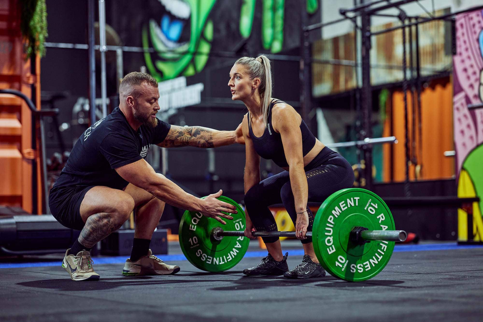 Coach Hall helping a client lifting a barbell